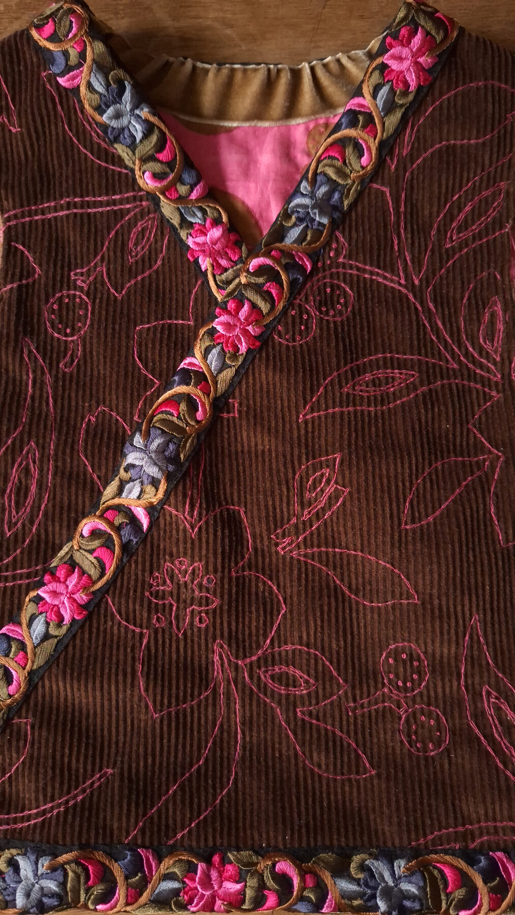 Detail hnědého oděvu s růžovou ruční výšivkou